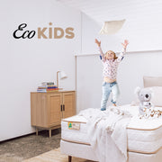 Child playing on a bed in a room with 'Eco Kids' branding.