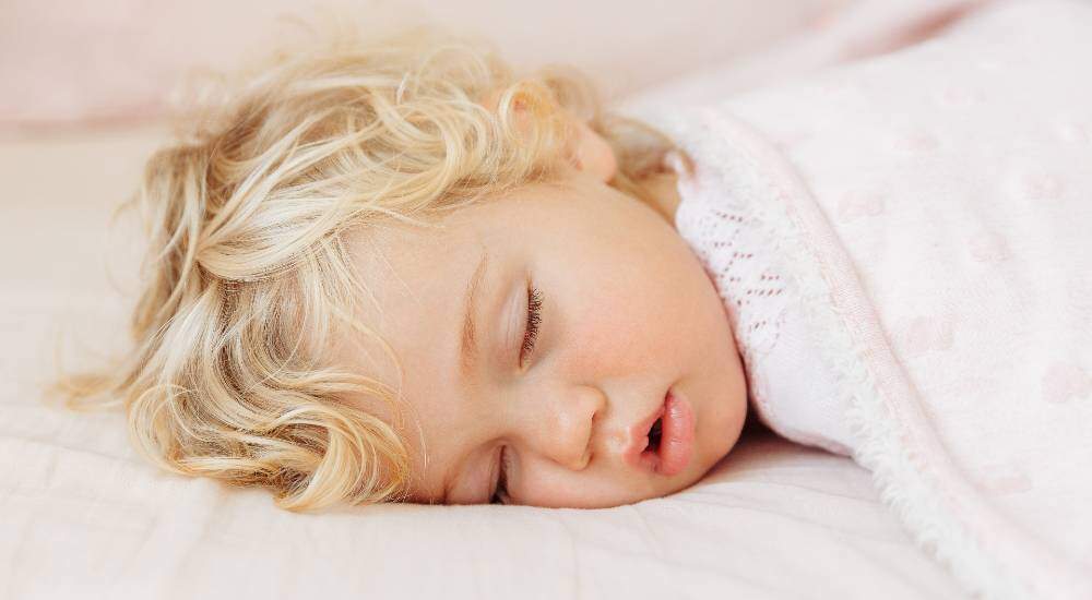 kid sleeping on the bed under pink blanket